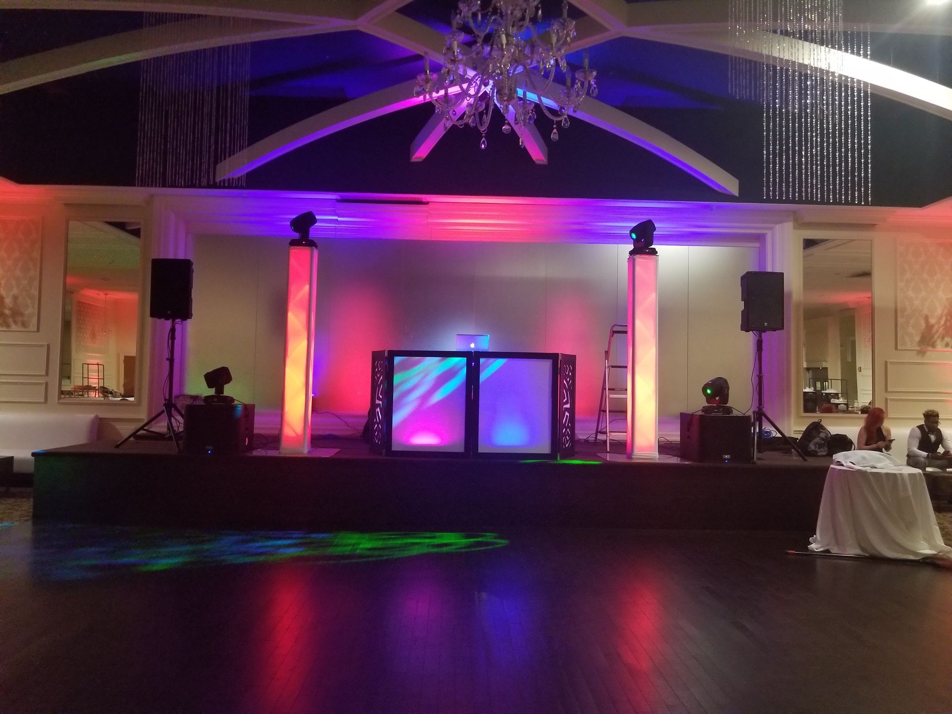 DJ stage setup lit with colorful lights. Speakers, lights, and DJ equipment on a stage. Elegant ballroom setting.