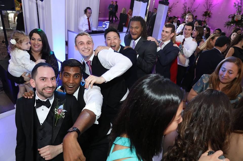 People celebrating at a party, dancing. Some wearing suits, smiling.