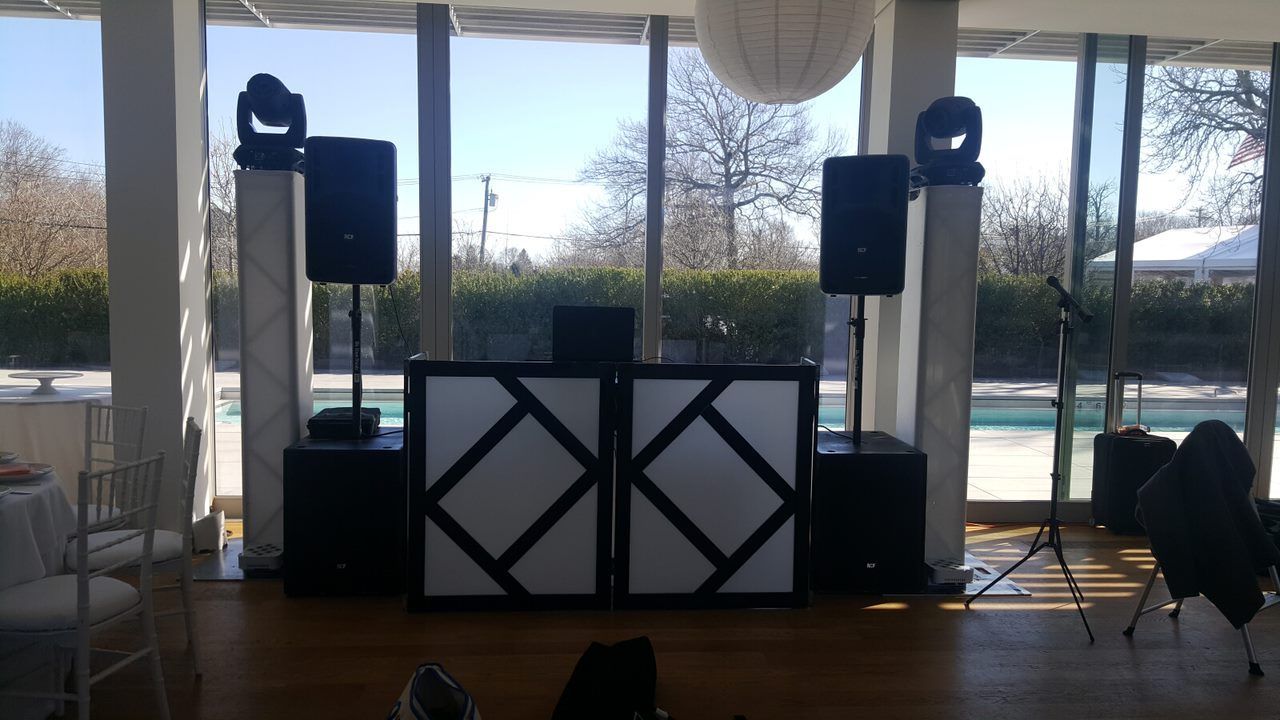 DJ setup with speakers, lights, and a white and black booth in front of large windows.