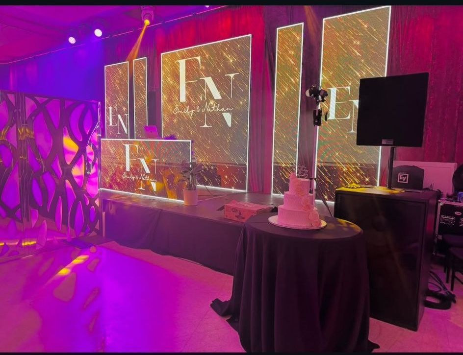 Event stage with logo displays, cake, and table, lit with purple and gold lights.