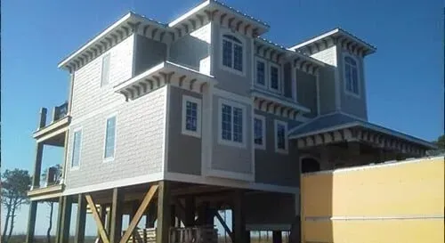 A large house is being built on stilts on a sunny day.