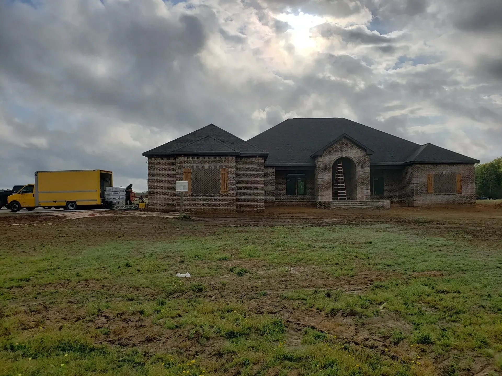 A large house is being built in a field with a yellow truck parked in front of it.
