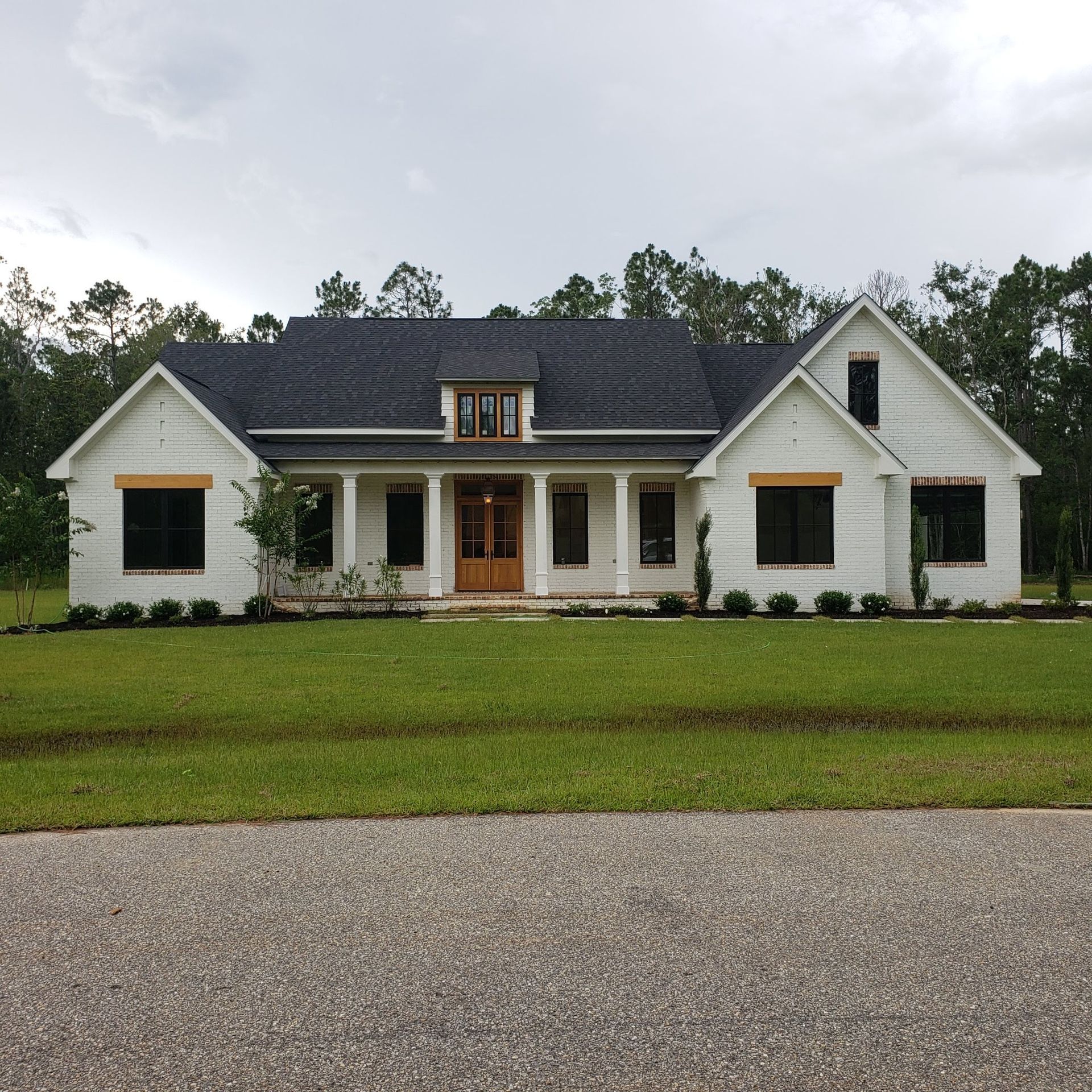 A white house with a black roof is surrounded by trees