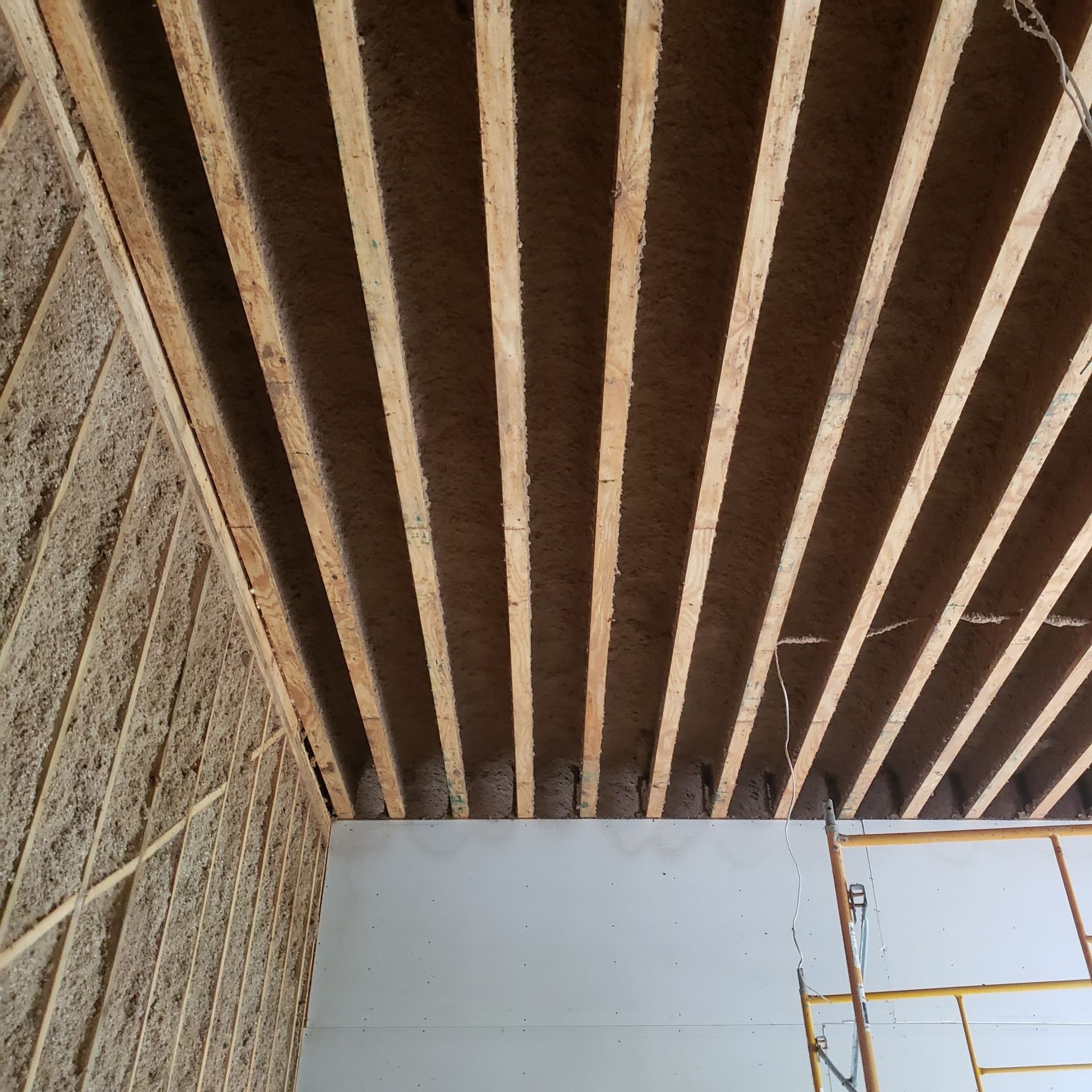 A ceiling with wooden beams and a scaffolding in the background