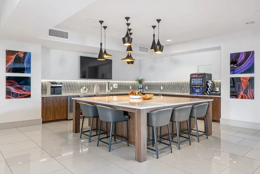 Modern kitchen with island, stools, and pendant lights; artwork on walls.
