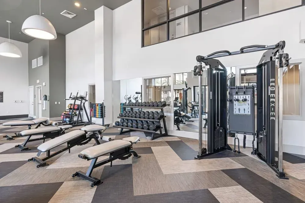 Gym with weight benches, free weights, and a cable machine. Gray and white interior.