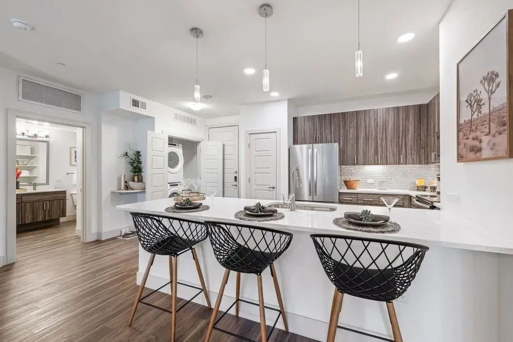 Modern kitchen with a breakfast bar, stainless steel appliances, and three black wire barstools.