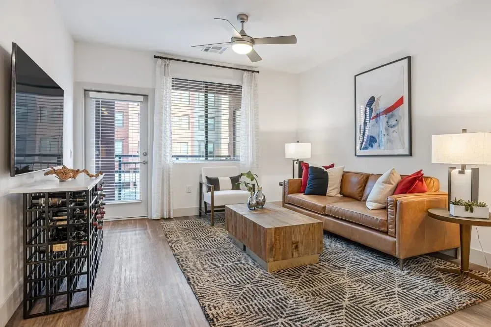 Living room with leather sofa, patterned rug, and art, near a balcony door and window.