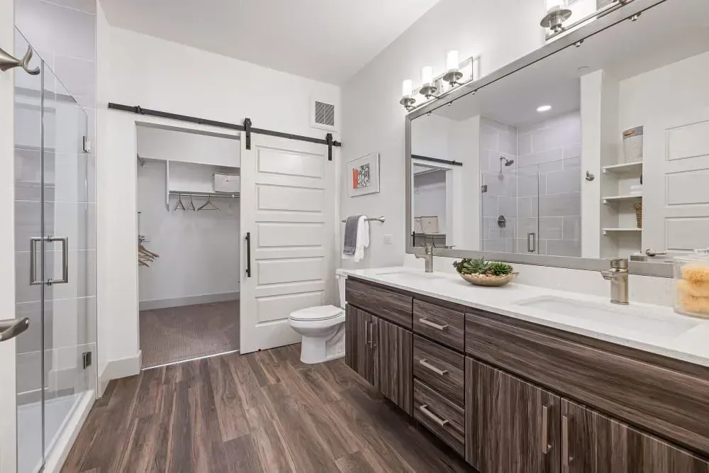Bathroom with a double vanity, shower, and sliding door leading to a closet. Modern design, wood floor.