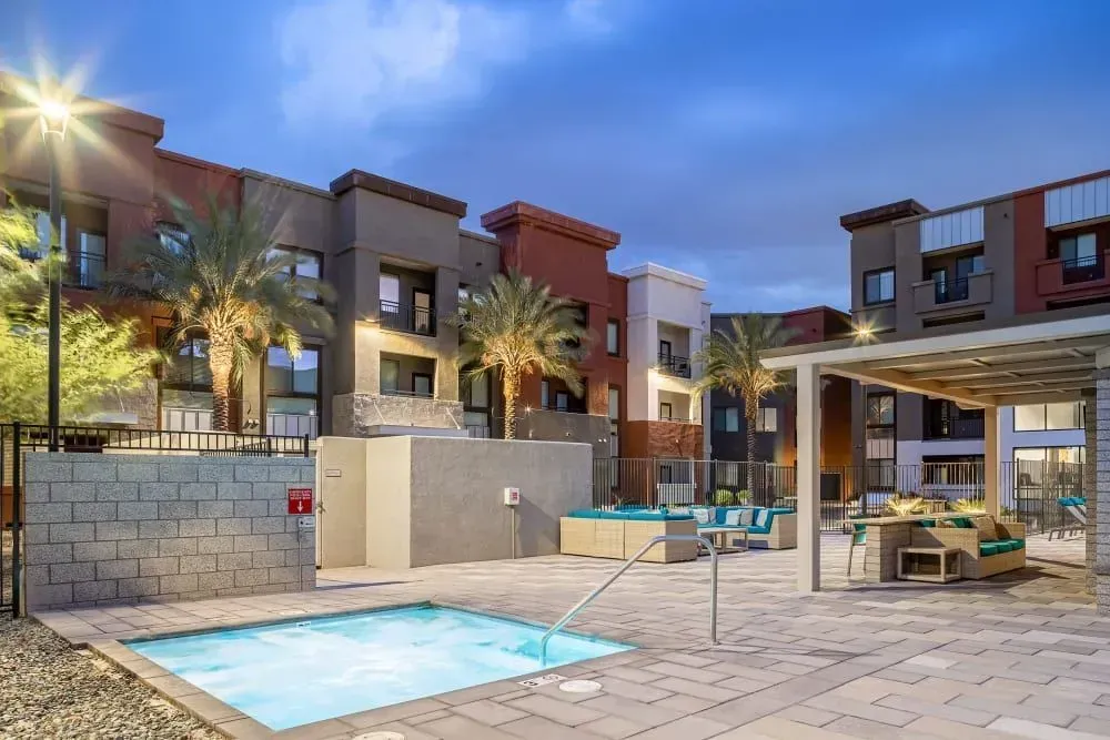 Apartment complex exterior with pool, lounge seating, and grill area at dusk.