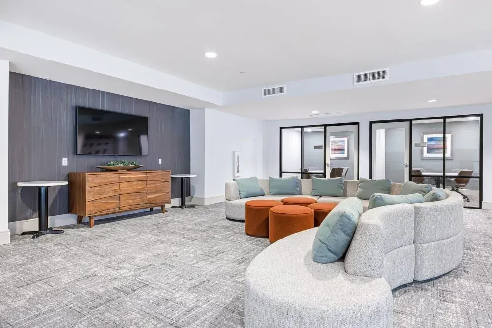 Lounge with curved sofa, TV on a wooden cabinet, and three glass-walled rooms.