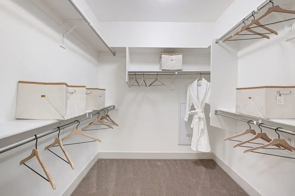 Empty walk-in closet with white walls, shelves, and neutral carpet. A white robe hangs in the middle.