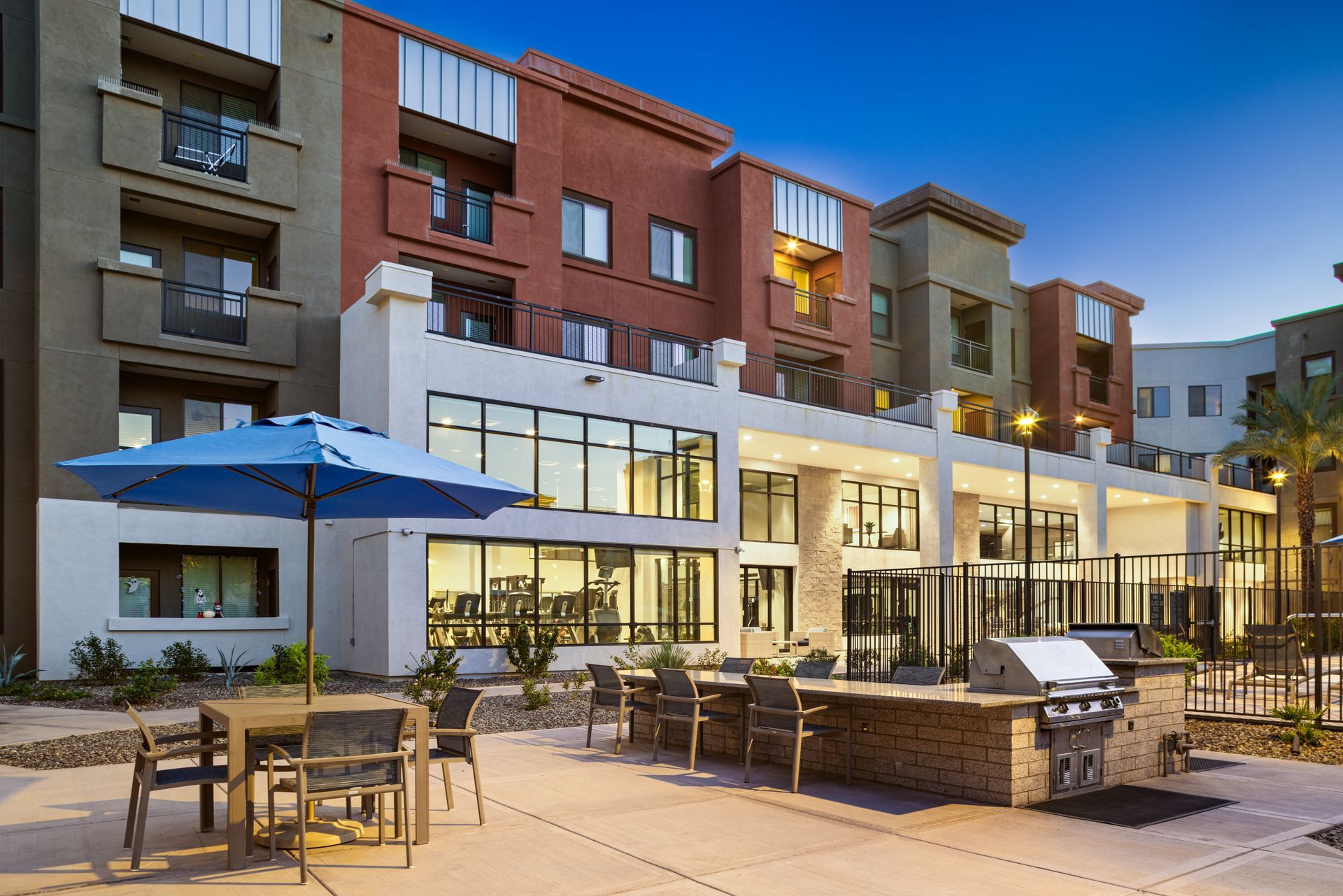 Outdoor patio with tables and umbrellas in front of a modern apartment building at dusk
