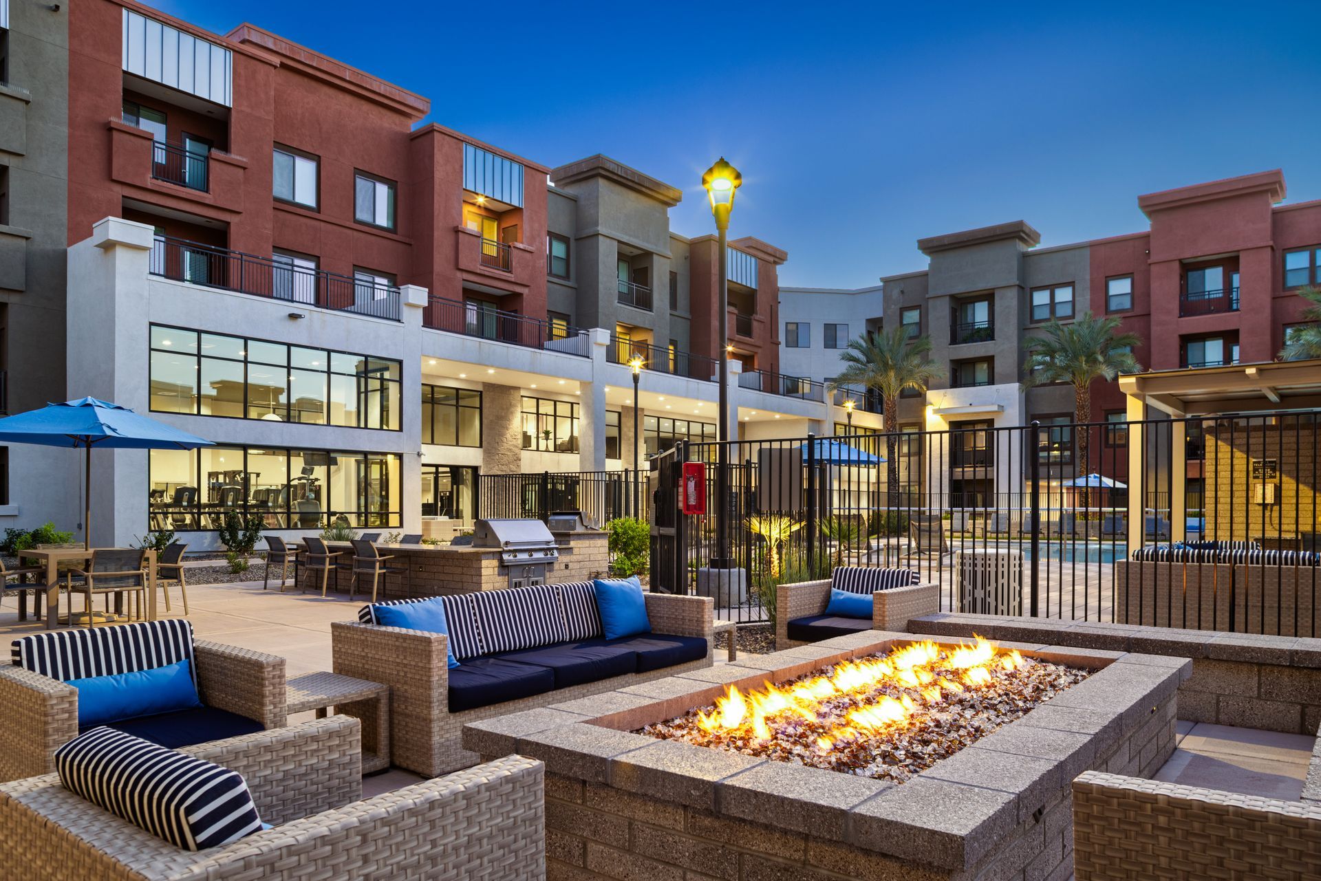 Modern apartment courtyard with fire pit, lounge seating, and lit outdoor dining area at dusk