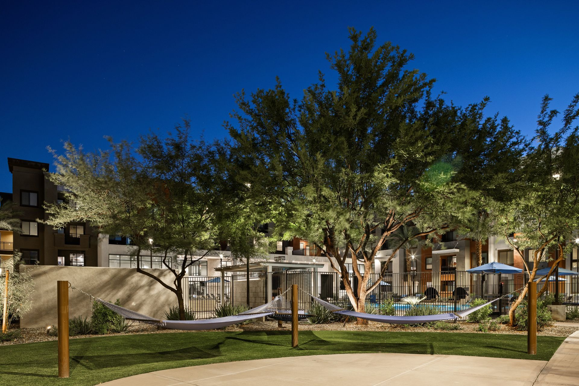 Courtyard with trees, lit walkways, and a modern apartment building at dusk