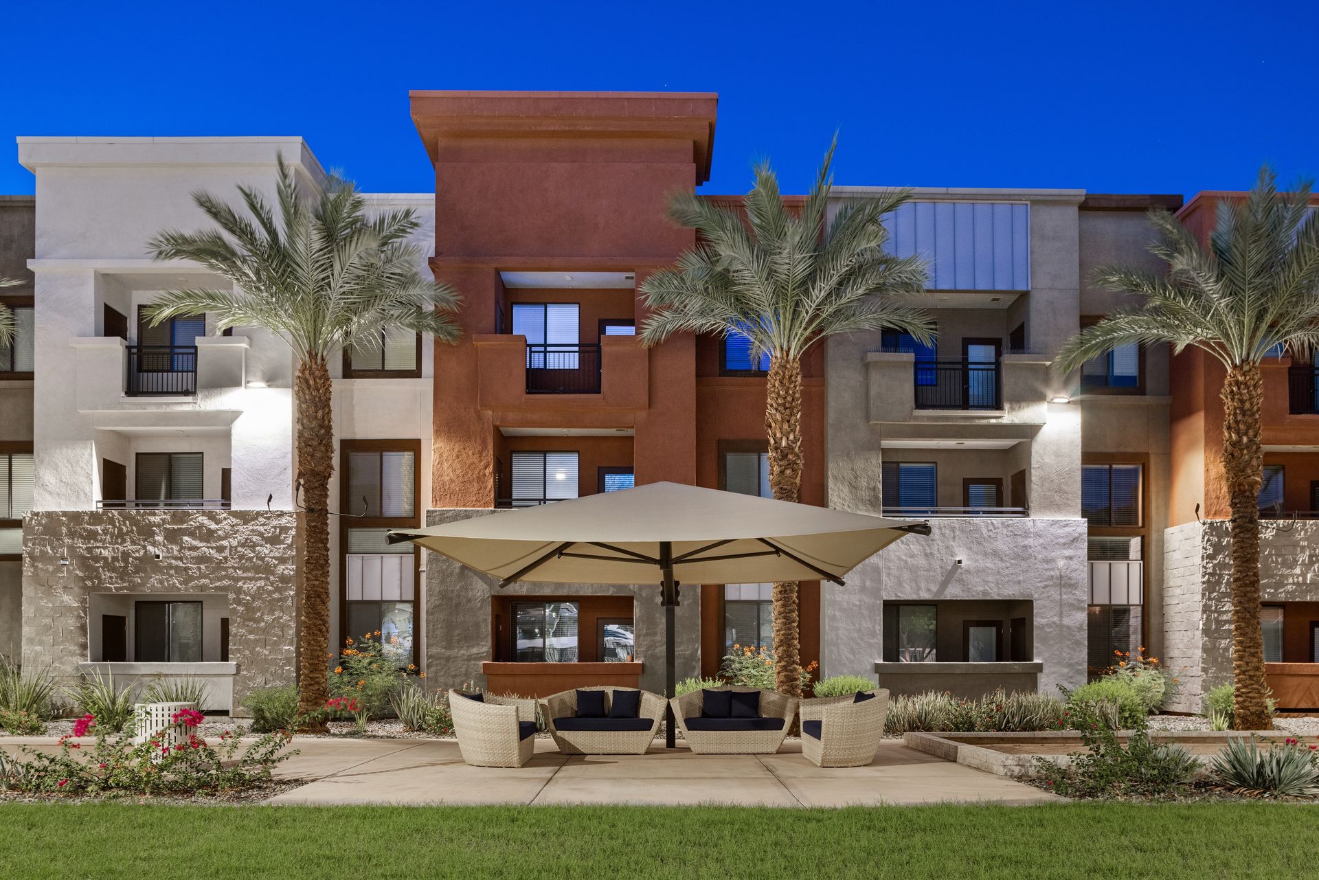 Modern apartment building with palm trees, stone accents, and a shaded patio in front