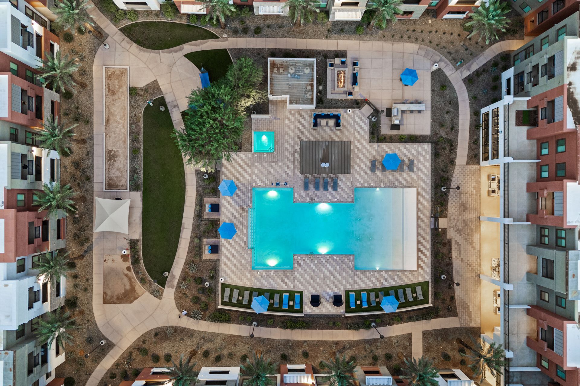 Aerial view of a resort-style courtyard with a turquoise swimming pool, lounge chairs, and surrounding apartment buildings