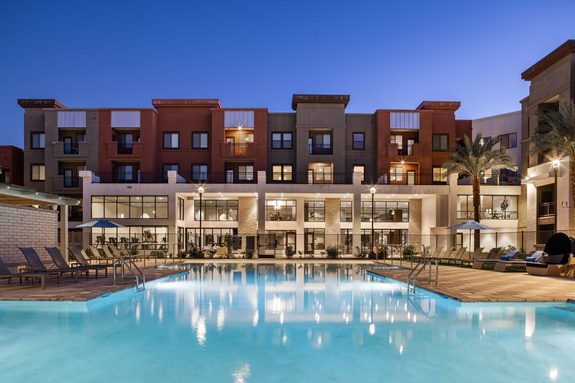 Luxury hotel pool at dusk with lit patio and apartment-style buildings behind it