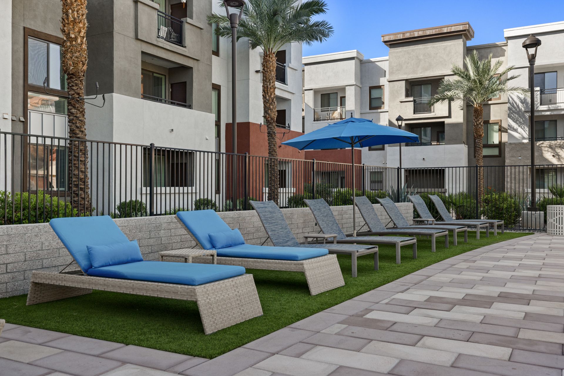 Poolside lounge area with blue chaise chairs, umbrellas, and apartment buildings nearby
