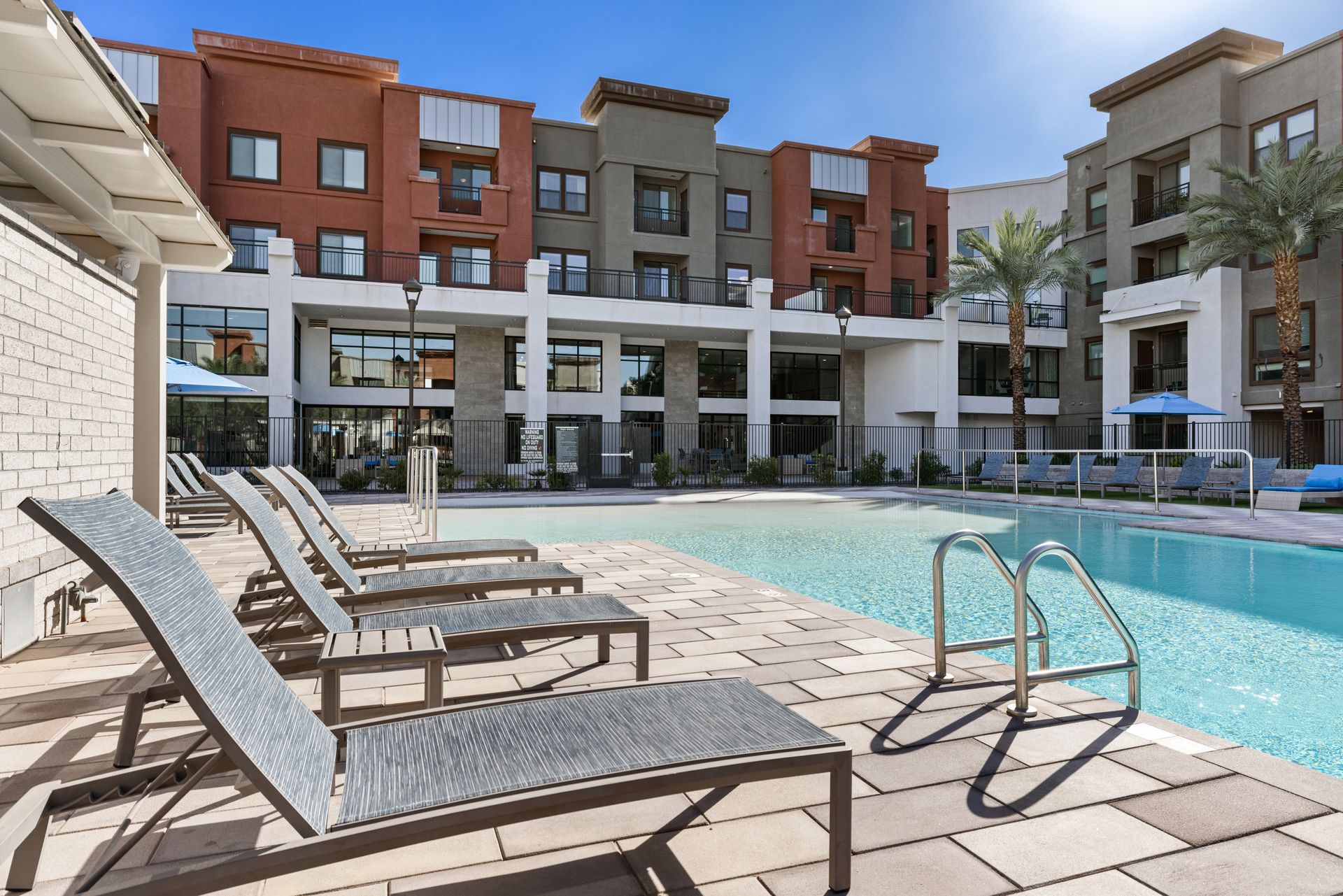 Outdoor apartment pool with lounge chairs and modern buildings surrounding it