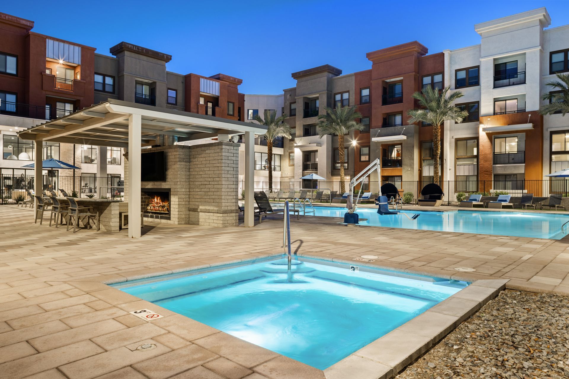 Modern apartment courtyard with a pool, hot tub, and lounge area at dusk