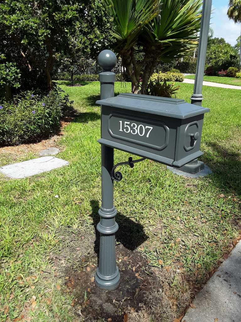 A gray mailbox is sitting in the grass next to a sidewalk.