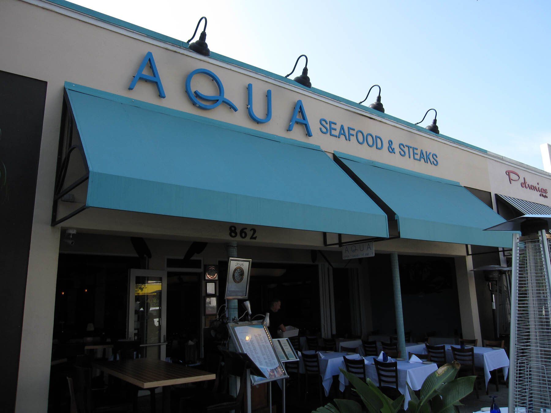 A restaurant called aqua seafood and steaks has a blue awning