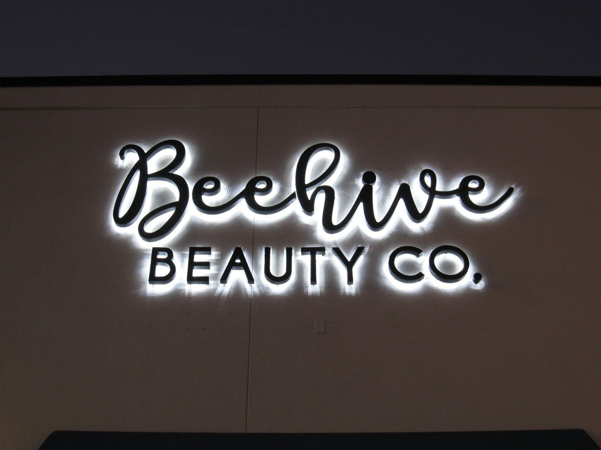 A sign for beehive beauty co. is lit up at night