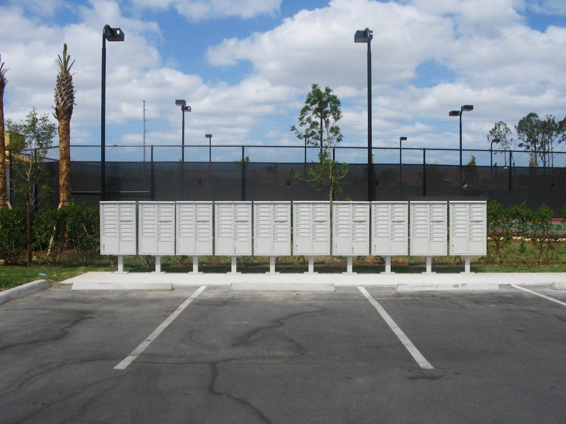 A row of mailboxes in a parking lot with a tennis court in the background