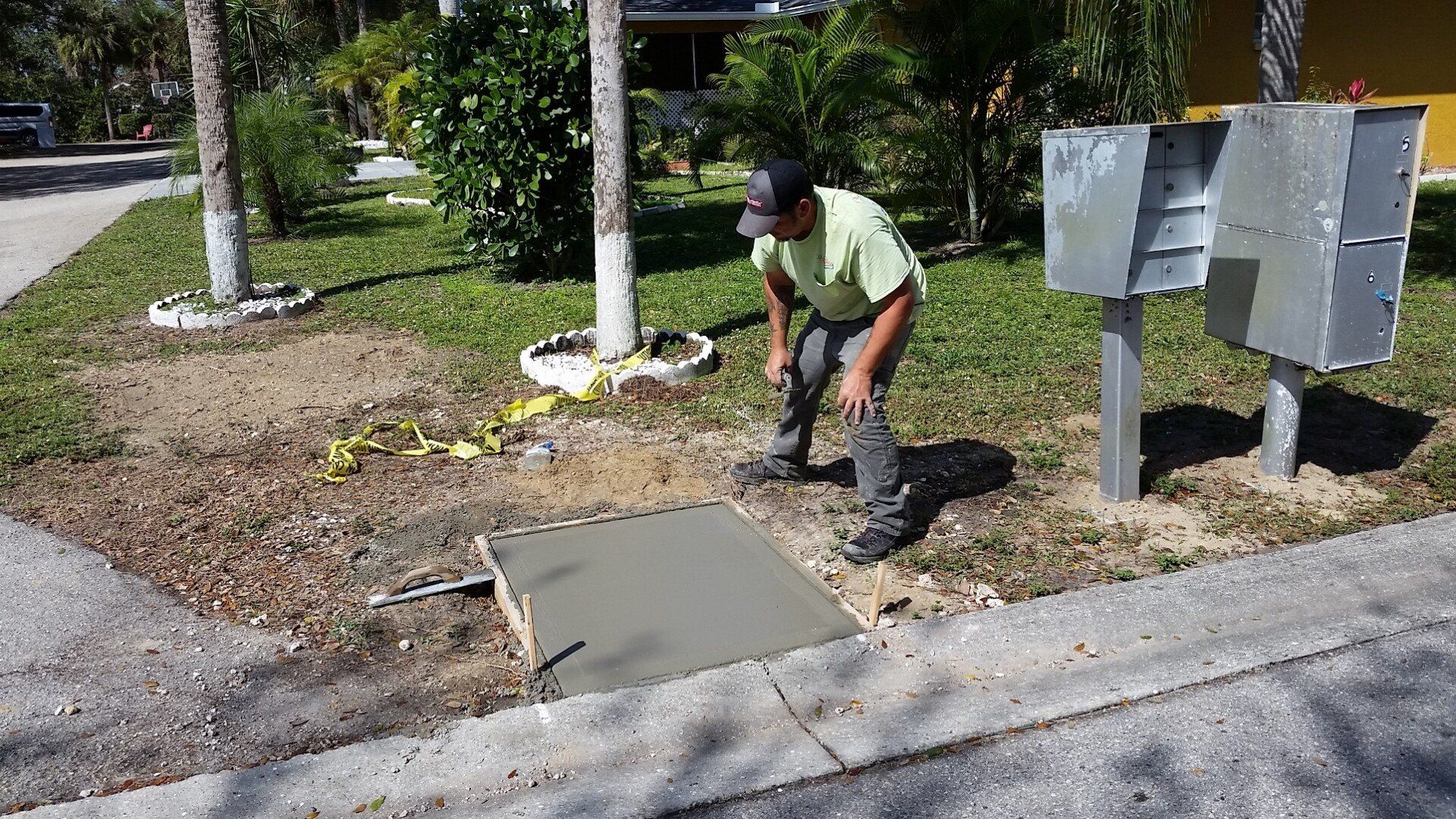 A man is working on a sidewalk next to a mailbox.