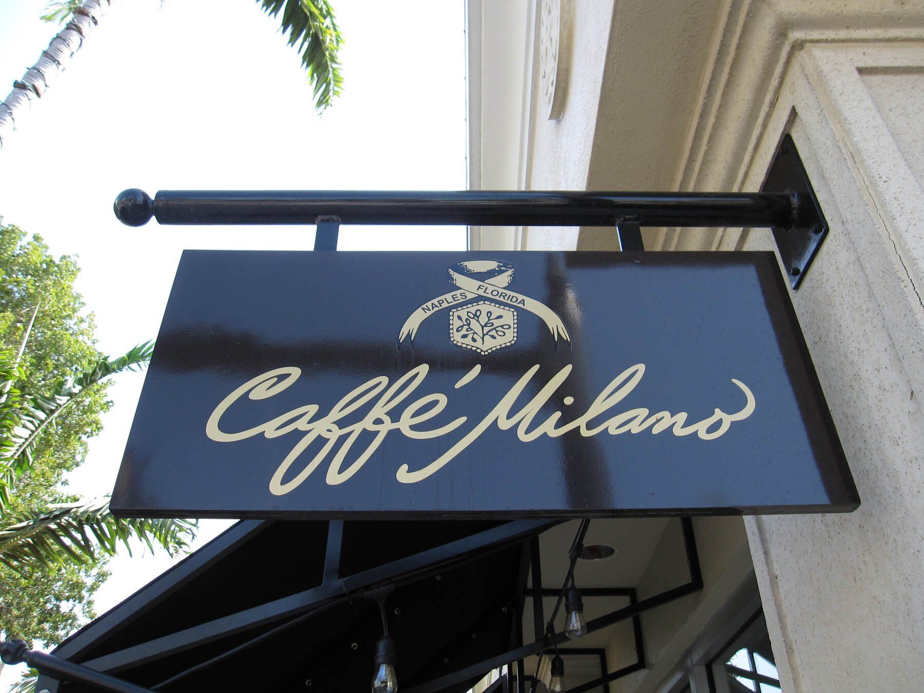 A sign for caffe milano hangs from the side of a building