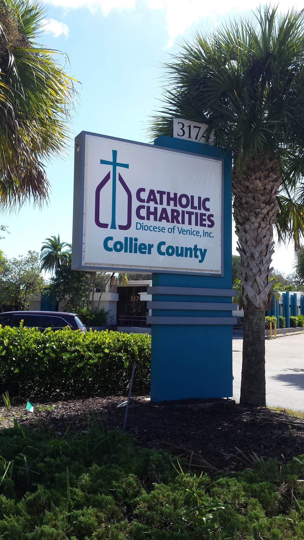 A blue and white sign for catholic charities collier county