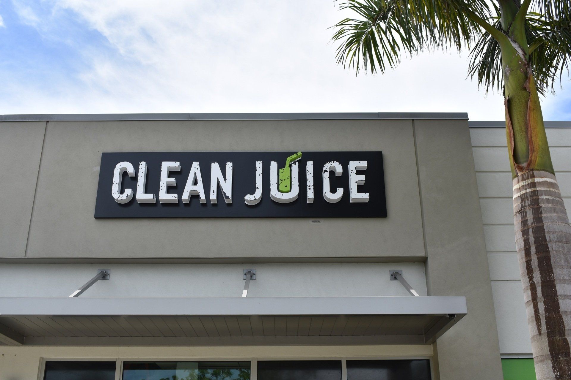 The front of a clean juice restaurant with a palm tree in the background
