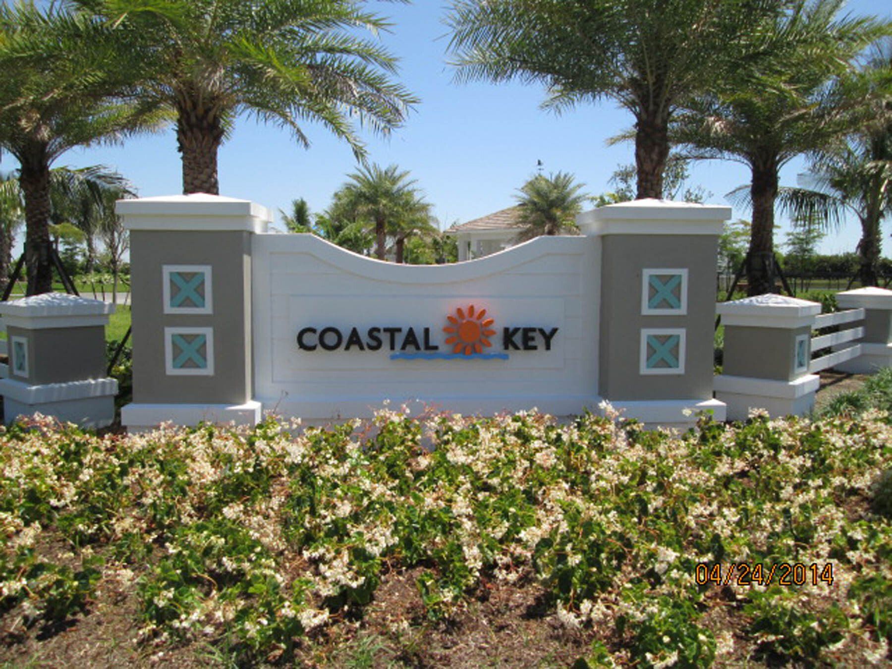 A sign for coastal key is surrounded by flowers and palm trees