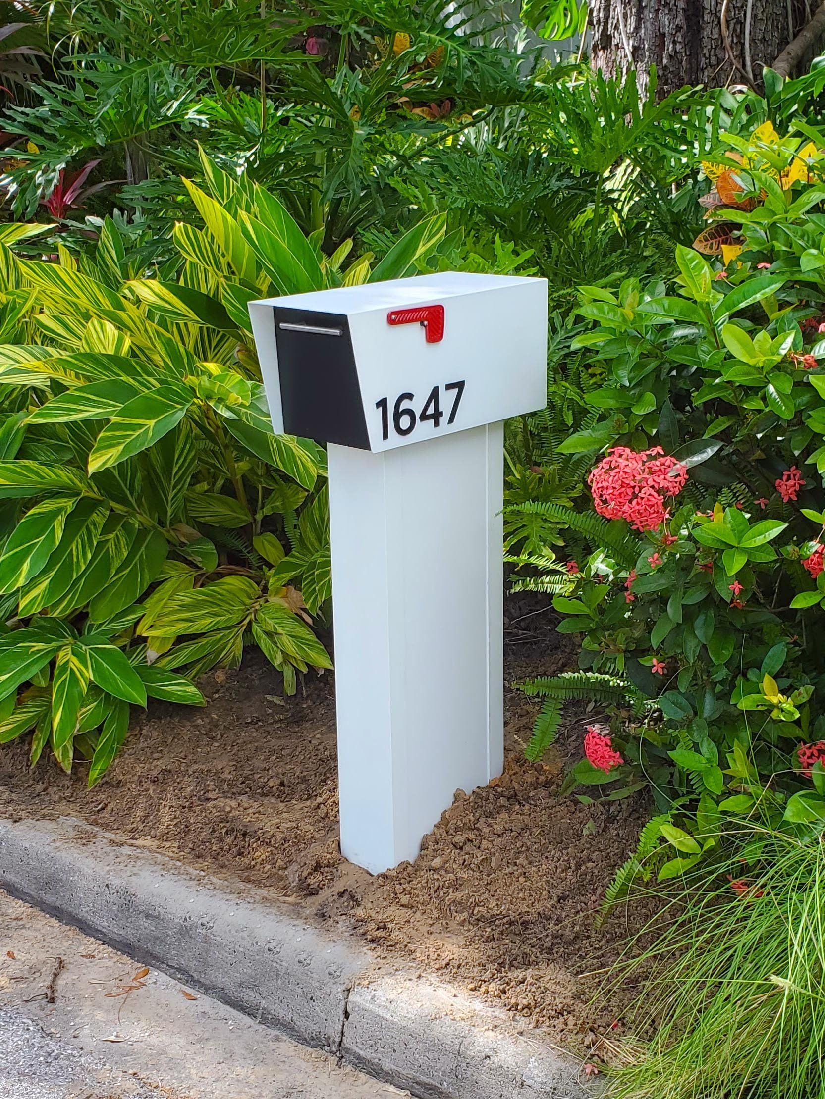 A white mailbox is sitting on the side of the road next to a bush.