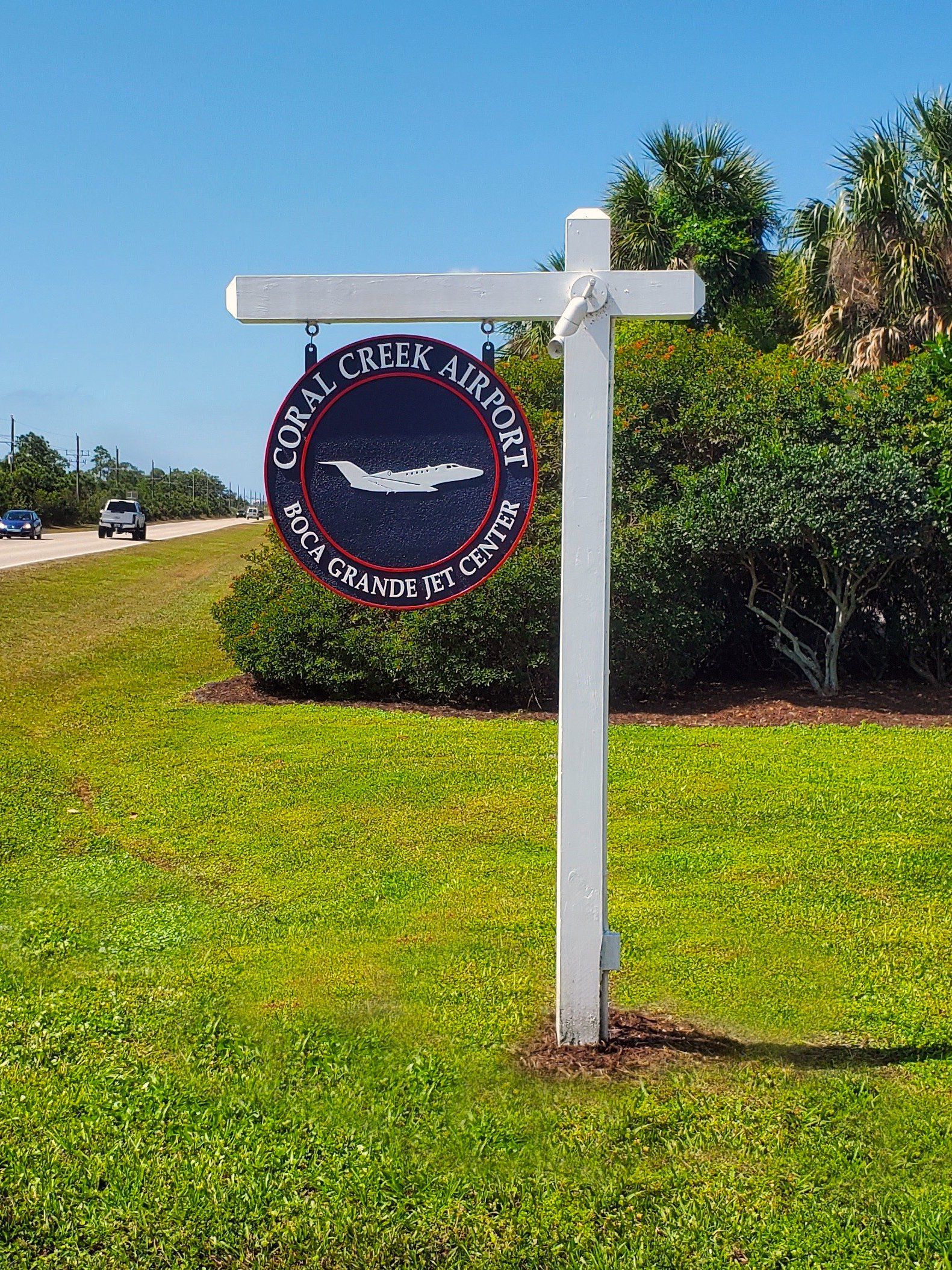 A sign is hanging from a white pole in the middle of a grassy field.