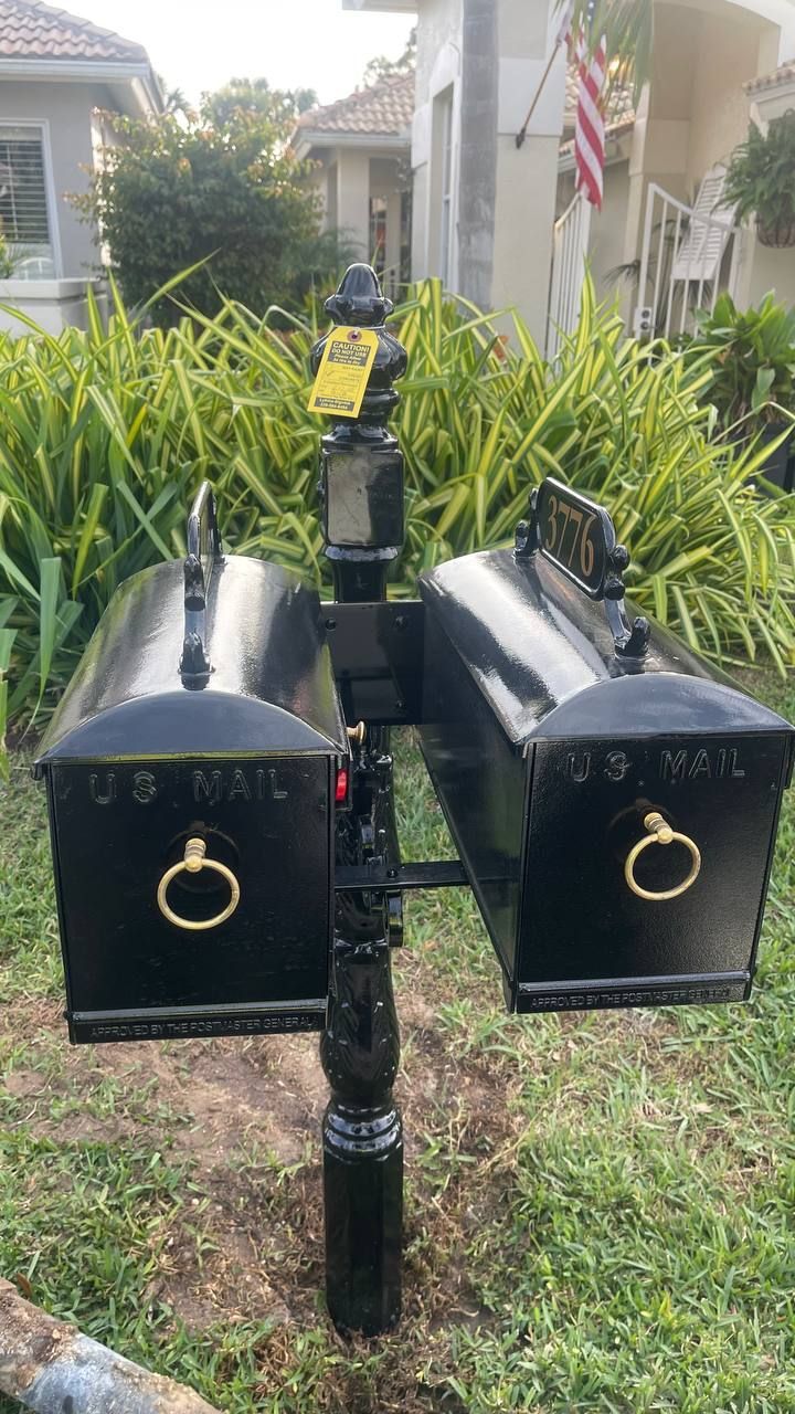 A black mailbox is sitting in the grass in front of a house.