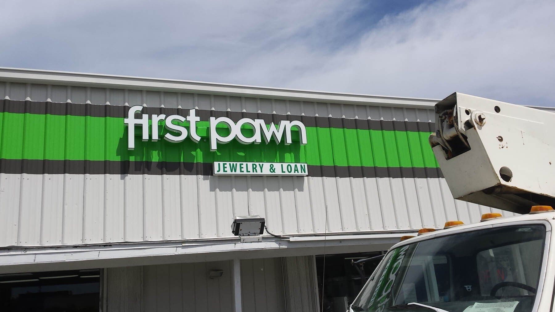 A white truck is parked in front of a building that says first pawn