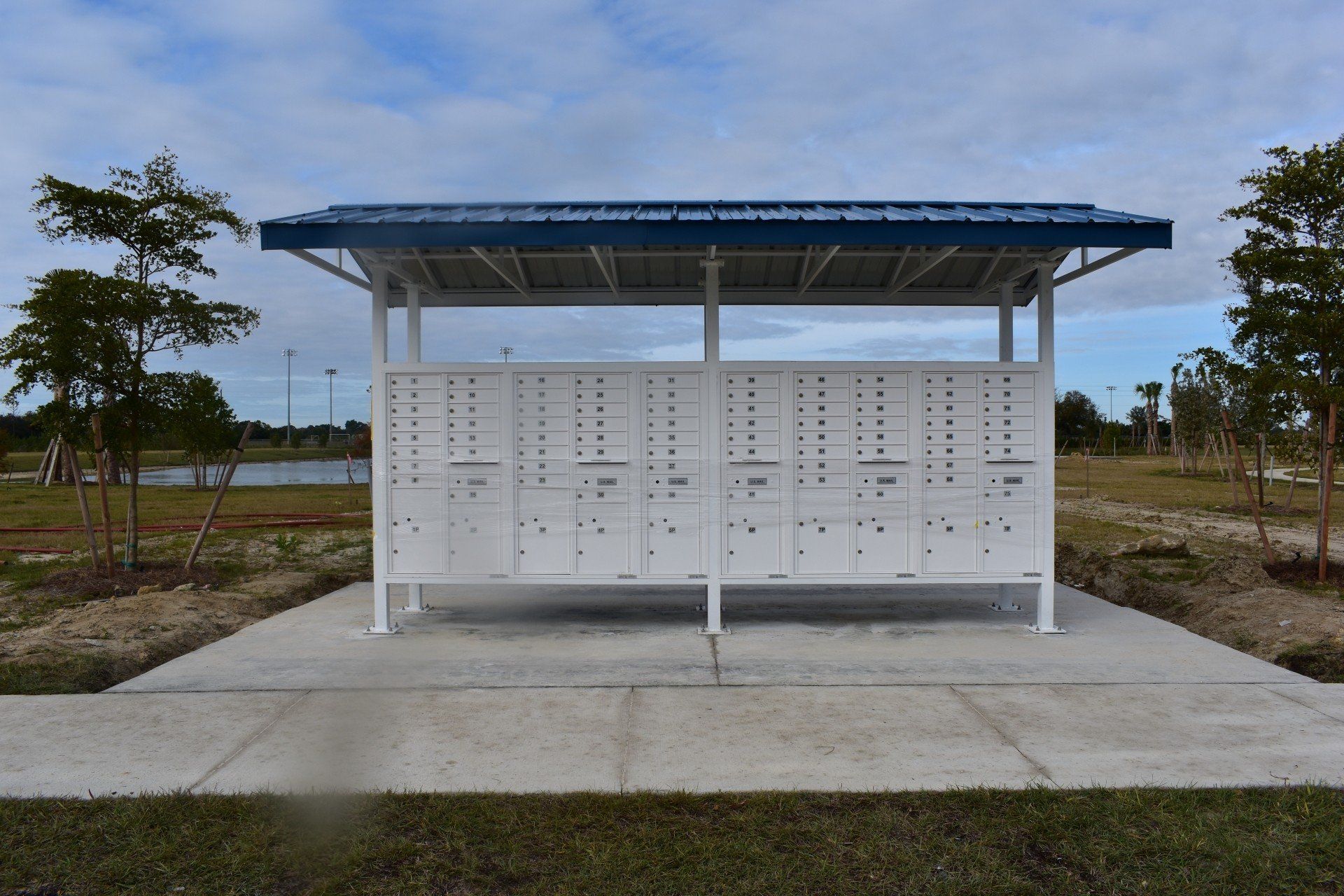A row of white mailboxes under a blue roof in a park