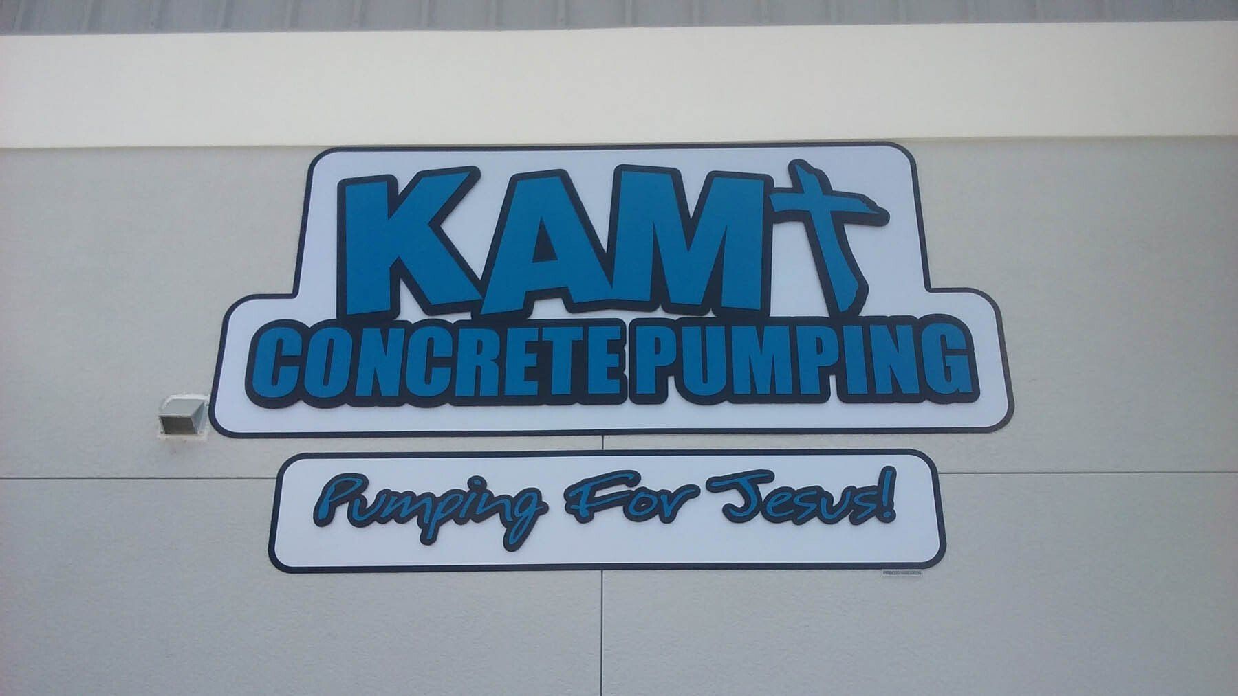 A sign for kamt concrete pumping hangs on the side of a building