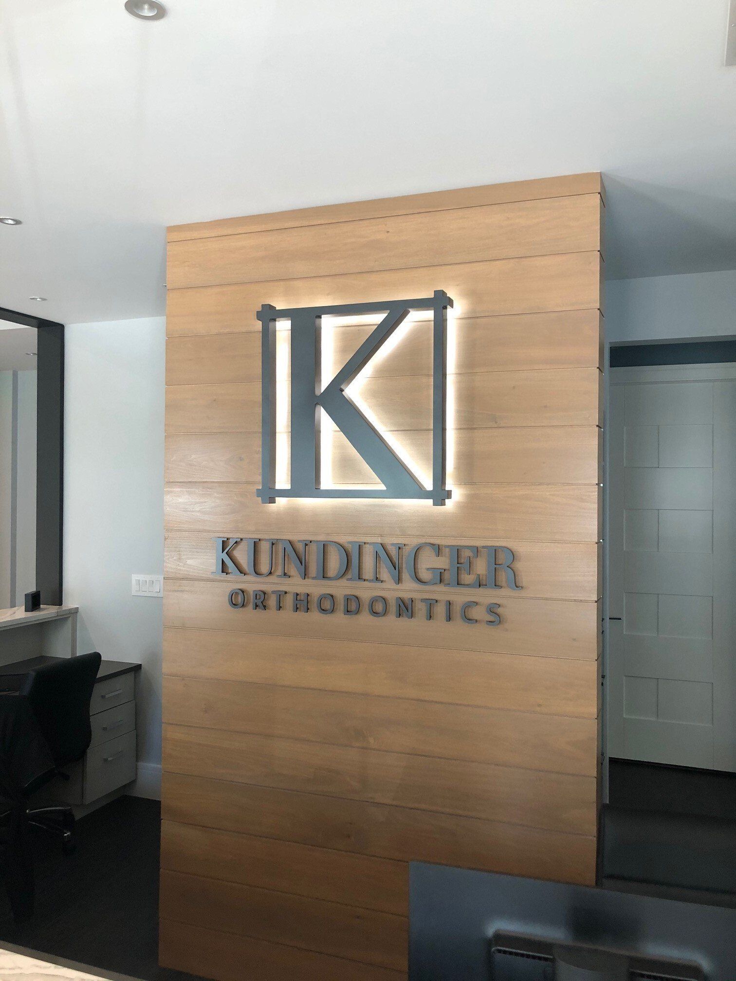 A sign for kindinger orthodontics is on a wooden wall.