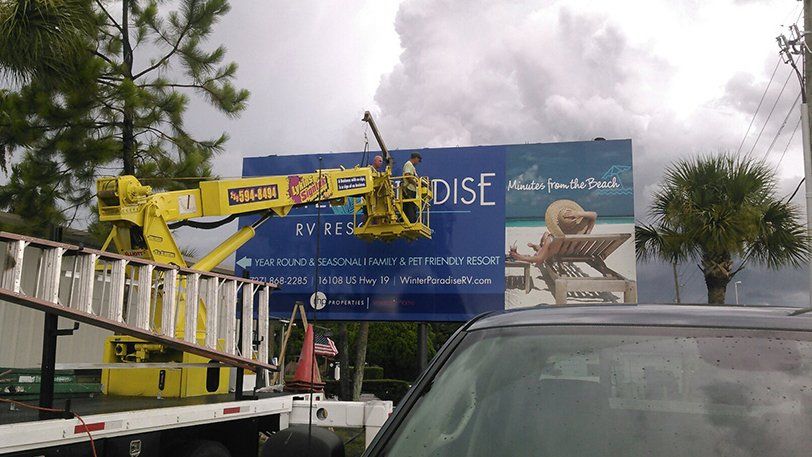 A large billboard with the word paradise on it is being installed by a crane.