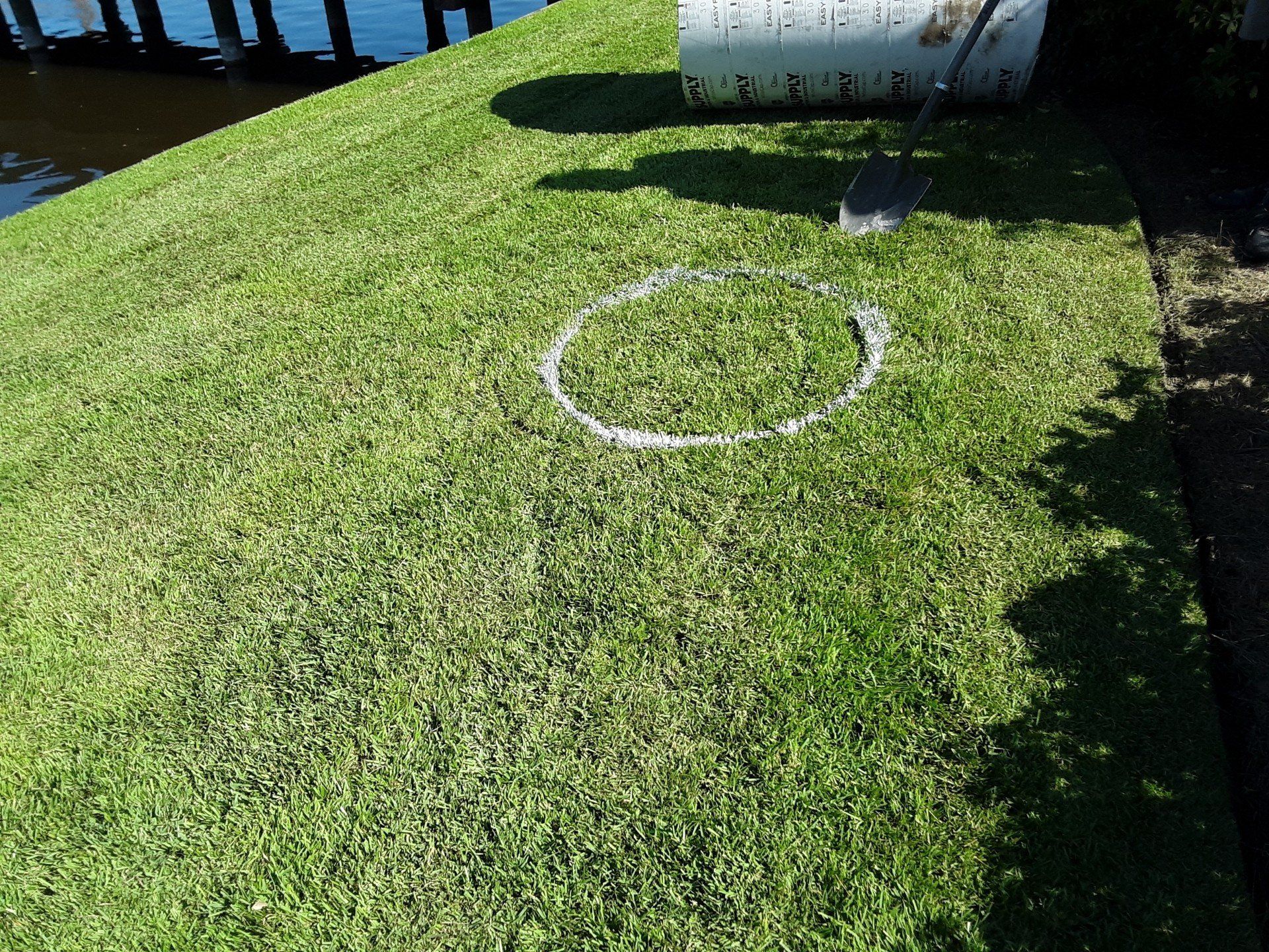 A person is drawing a circle in the grass with a shovel.