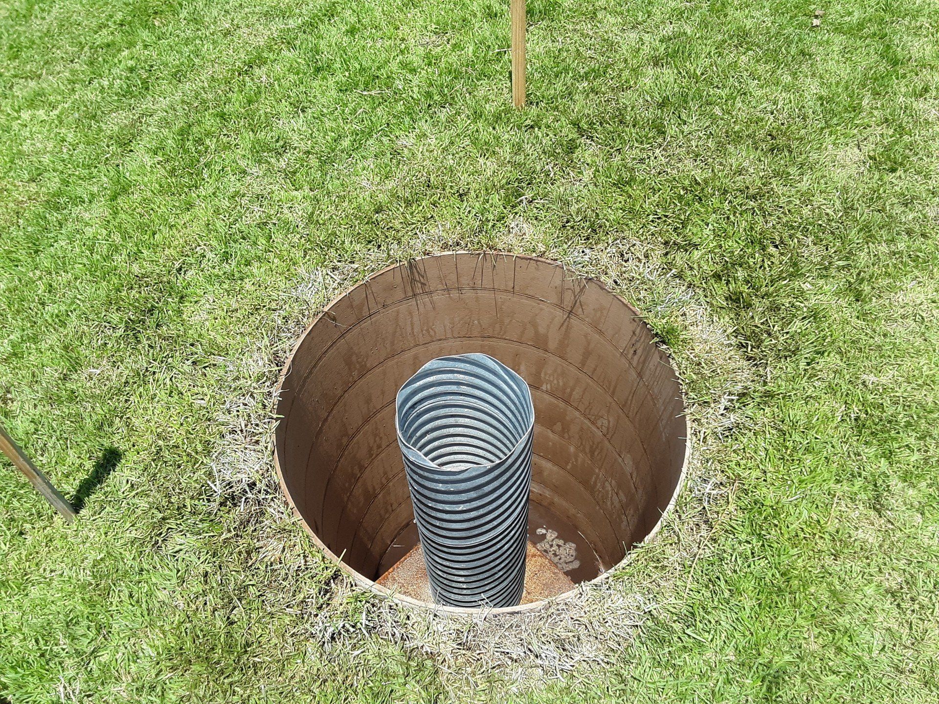 A large pipe is sitting in the middle of a hole in the grass.