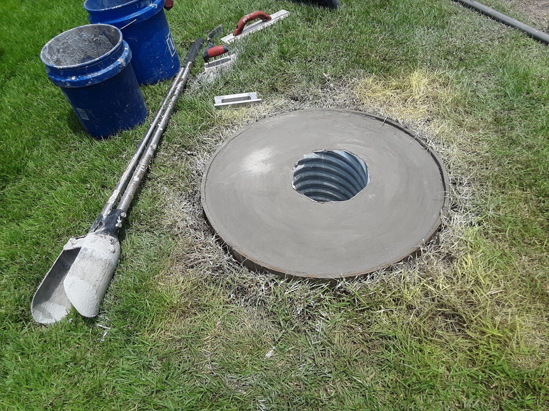 A manhole cover with a hole in it is being built in the grass.