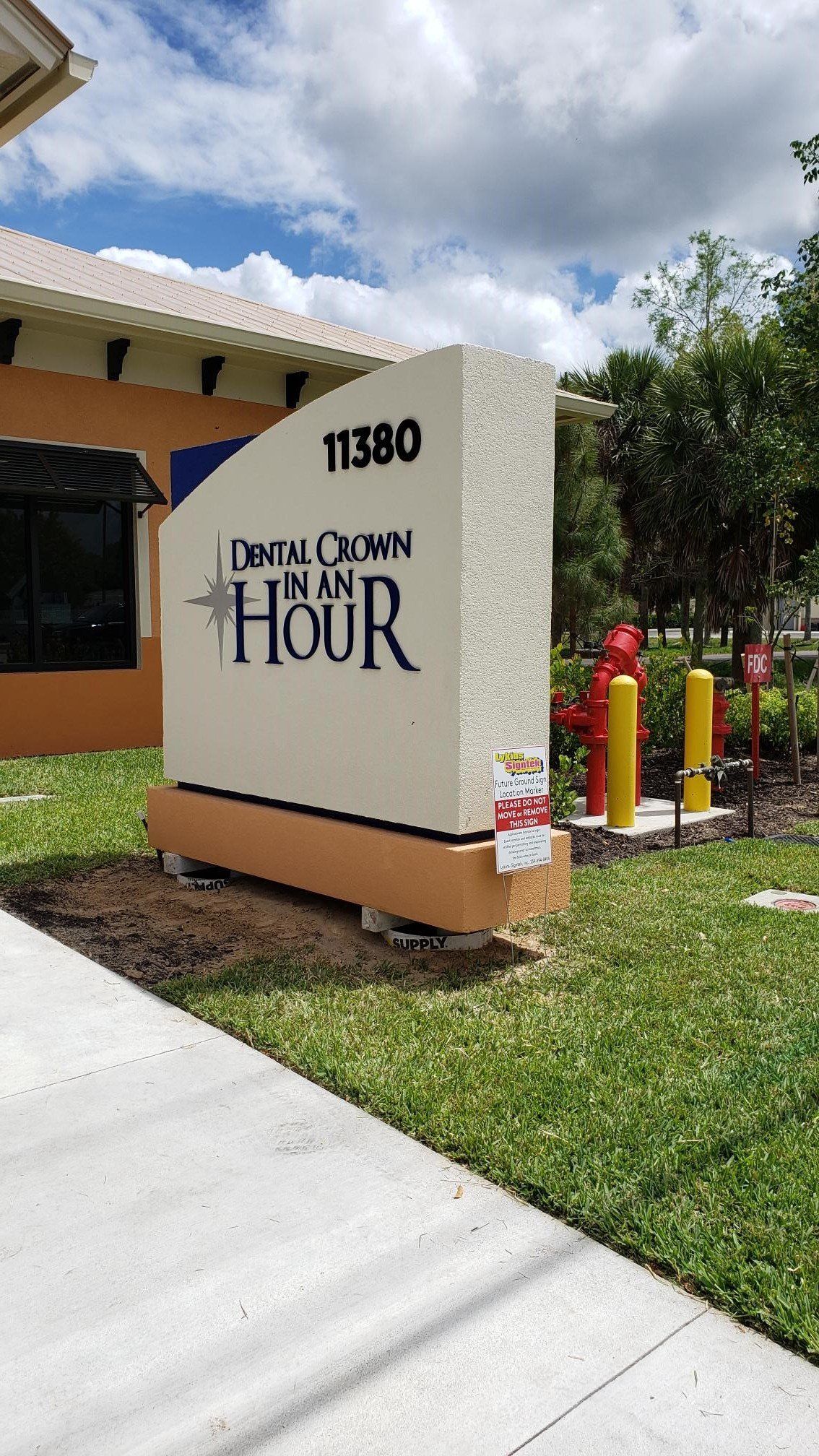 A large white sign is sitting in the grass in front of a building.
