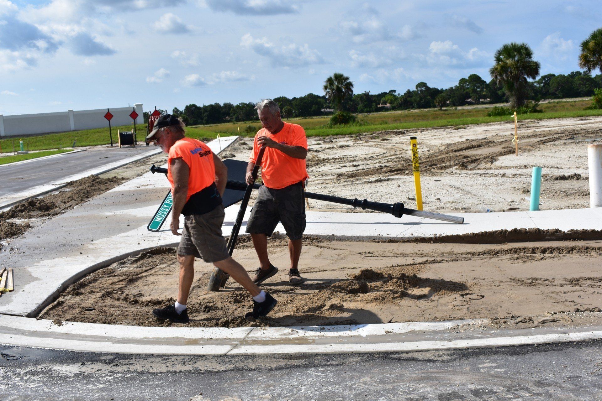 Two men are working on a sidewalk and one is pushing a wheelbarrow.