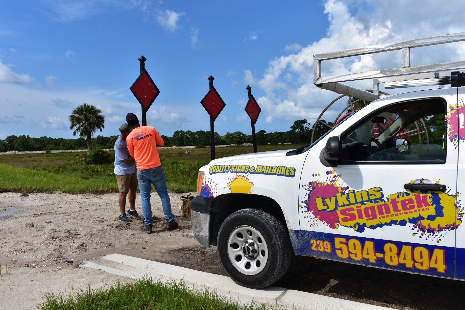 A couple standing next to a truck that says lynch 's signtek