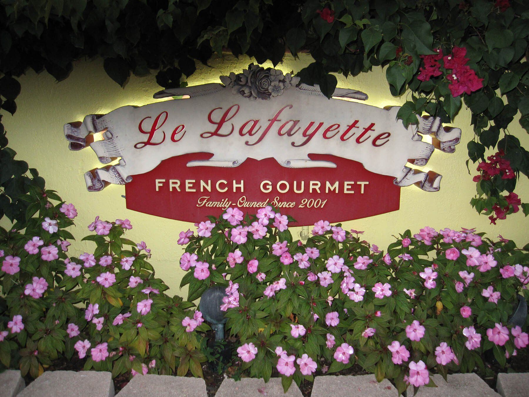 A sign for le lafayette french gourmet is surrounded by pink flowers