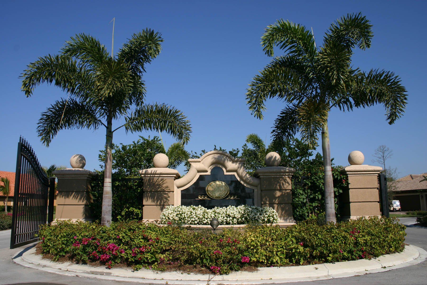A gated entrance with palm trees and flowers